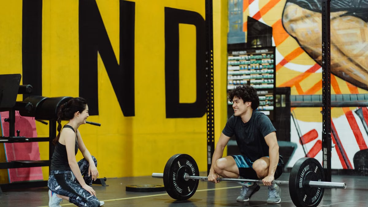 Two young adults in a gym participating in a weightlifting session, sharing a positive moment.